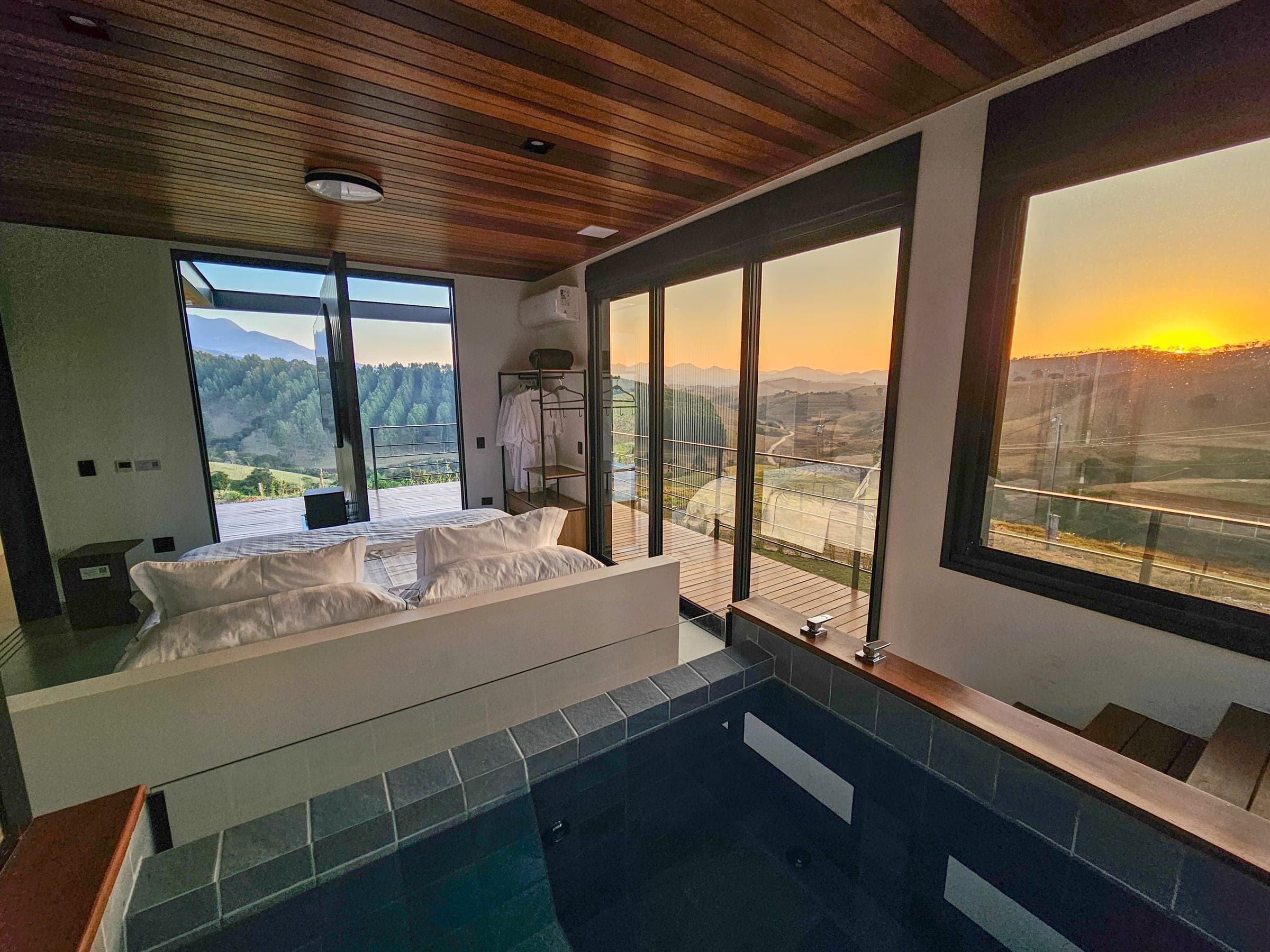 Quarto do Solarium 2 com cama, SPA interno e janelas abertas para o pôr do sol